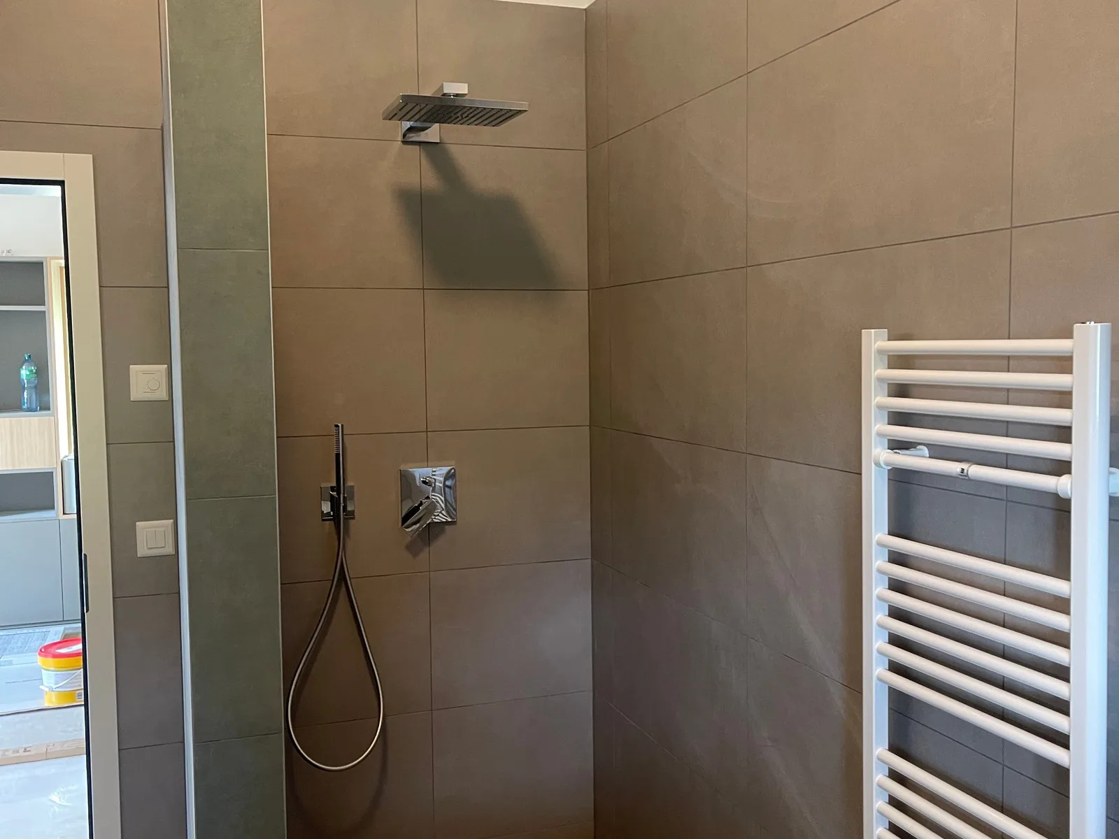Douche avec colonne encastrée chromée sur grès cérame taupe grand format, bande verticale décorative
